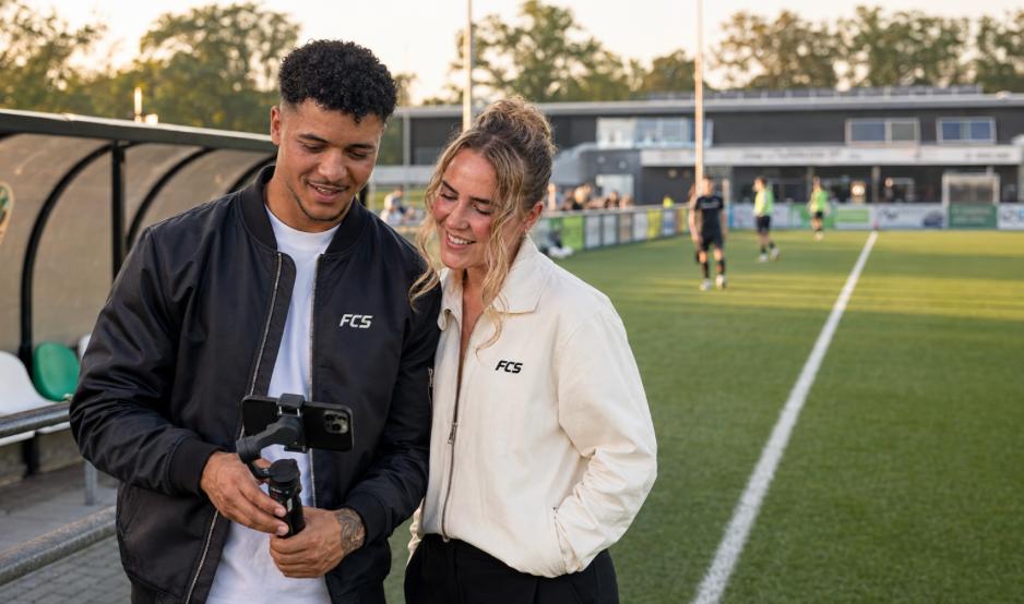 Jonathan en Dirkje van FC Socials kijken lachend naar camerabeelden langs het voetbalveld